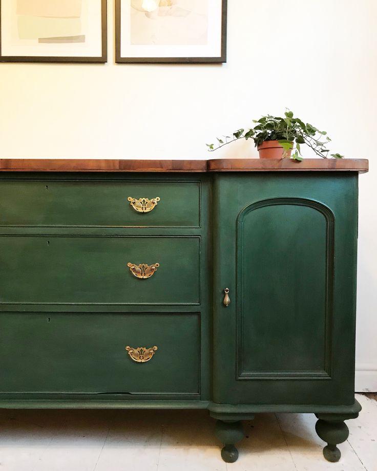 a green dresser with two pictures on the wall and a potted plant sitting on top