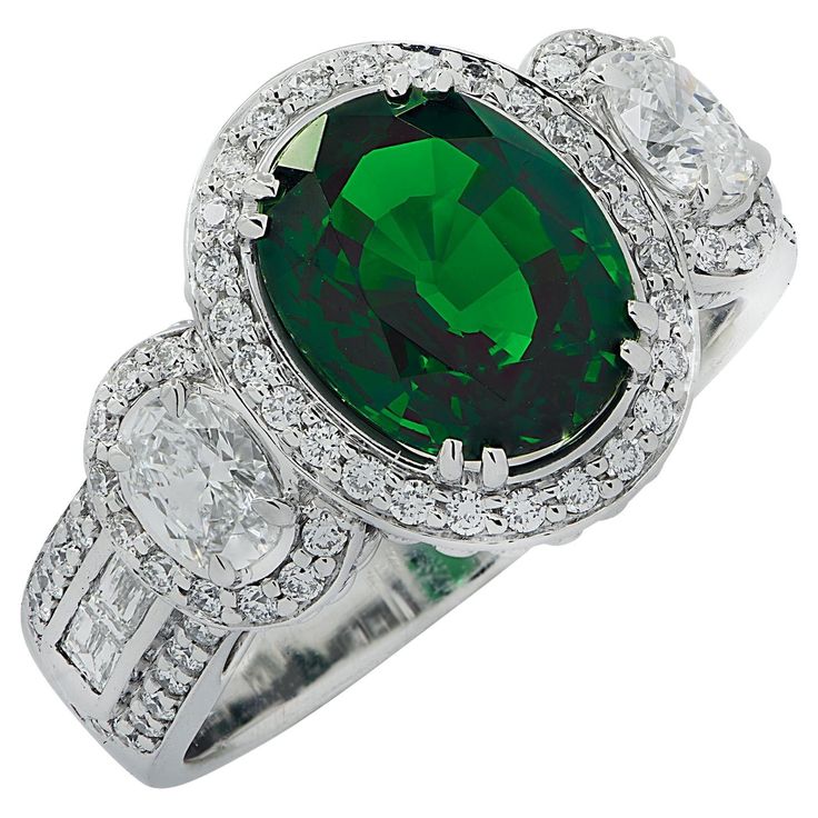 Spectacular Vivid Diamonds ring crafted in 18 karat white gold showcasing a stunning rich green oval cut Tsavorite weighing 3.38 carats, accented by two round oval cut diamonds weighing approximately .40 carats total, G color, VS clarity, and 84 round brilliant and baguette cut diamonds weighing approximately 1 carat total, F-G color VS clarity. The Tsavorite is surrounded by a diamond halo, and is flanked by two oval cut diamonds laced with round brilliant cut diamonds. The shank is adorned wit Color Stone Ring, Ornate Ring, Beautiful Tiaras, Green Oval, Diamonds Ring, Baguette Cut Diamond, Expensive Jewelry, Ring Crafts, Rich Green