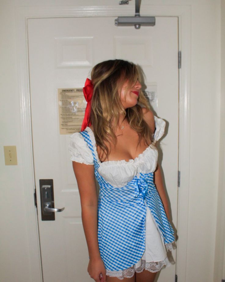 a woman wearing a blue and white dress standing in front of a door with a red bow on her head