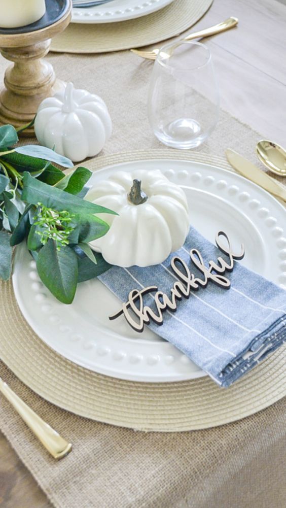 a place setting with pumpkins and greenery on the table, along with napkins