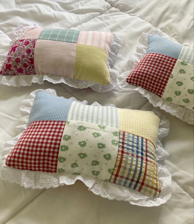 three decorative pillows on a bed with white lace trimmings and colorful plaid patterns