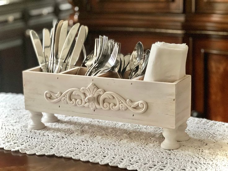 a wooden box filled with silverware on top of a white doily covered table