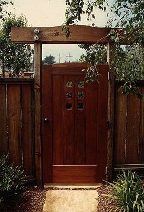 a wooden door is in the middle of a small garden area with plants and trees