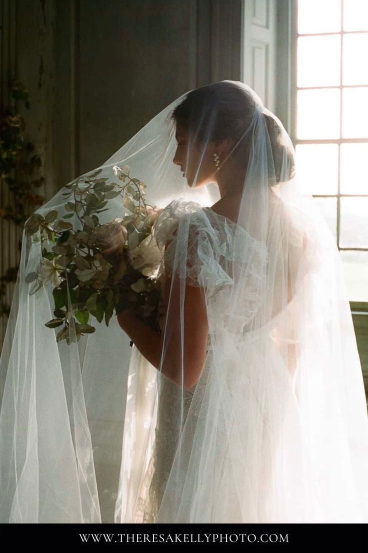 a woman in a white wedding dress holding a bouquet of flowers and wearing a veil