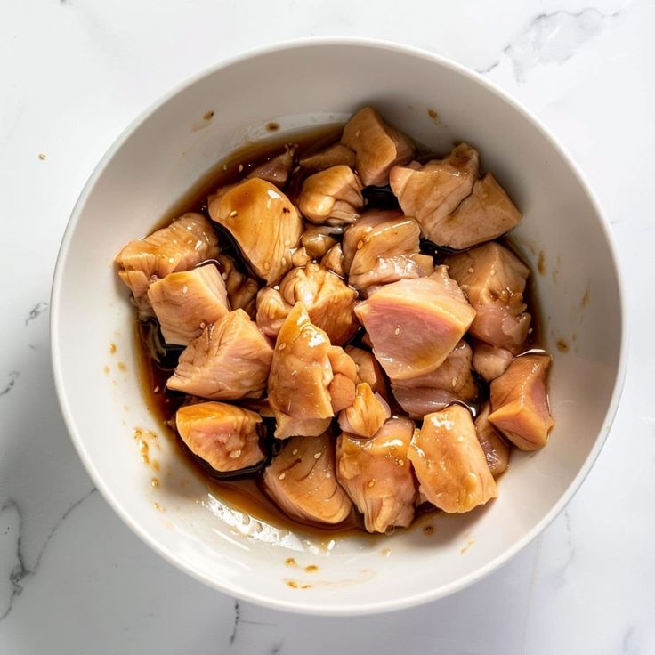 a white bowl filled with meat and sauce on top of a marble countertop next to a knife