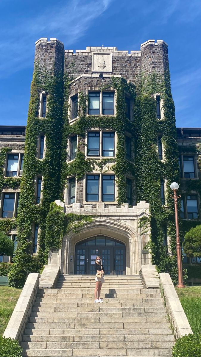 a woman standing in front of a large building with ivy growing on it's walls