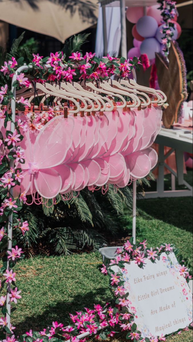 a bunch of pink flowers are hanging from a rack in the grass near some tables