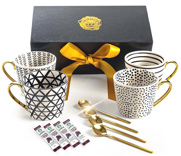 four coffee mugs with gold handles and matching spoons in front of a gift box