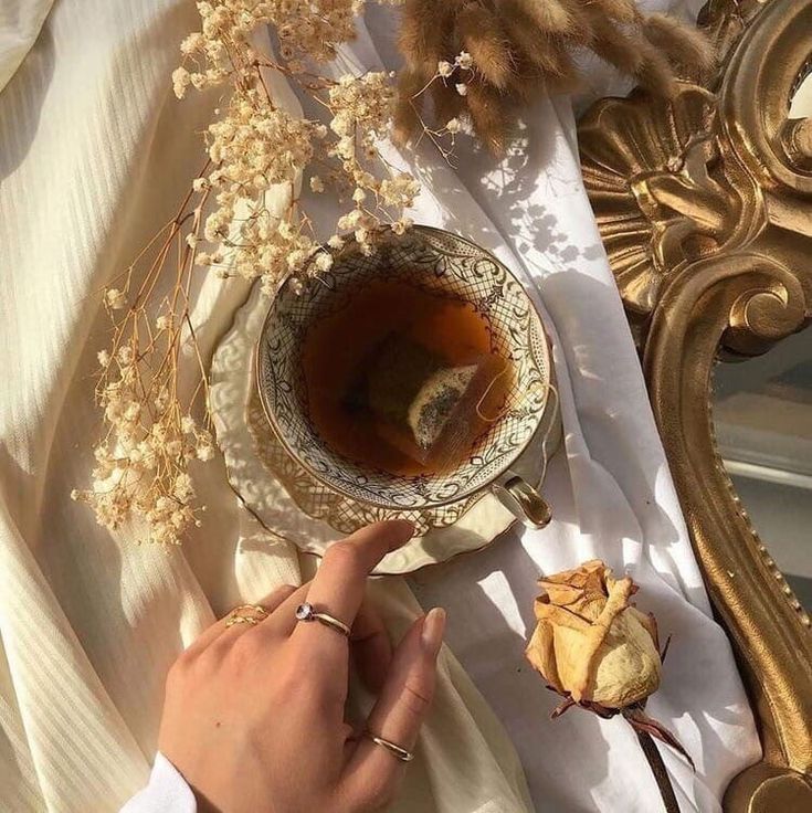 a person is holding a spoon near a tea cup on a table with dried flowers