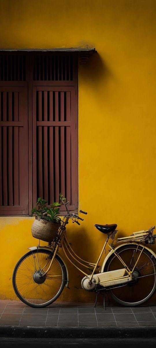 a bike parked next to a yellow wall with red shutters and a planter