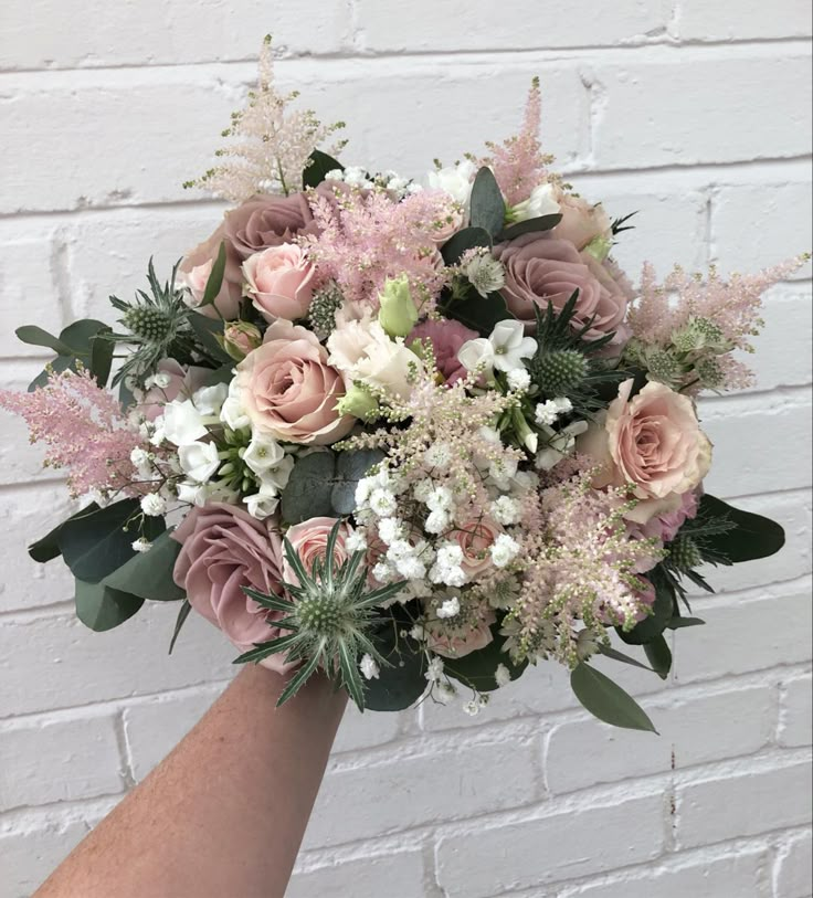 a bouquet of pink and white flowers is held up against a brick wall by someone's hand