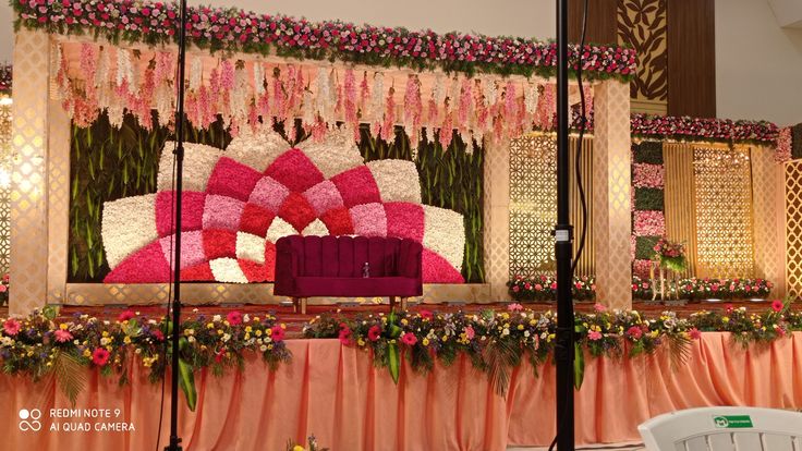 a stage set up for a wedding ceremony with pink and white flowers on the wall