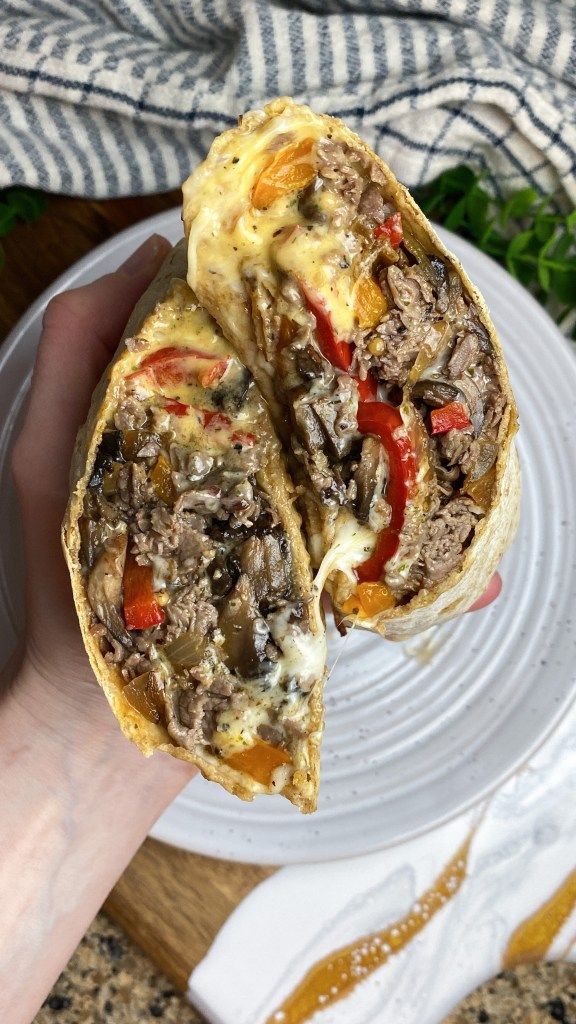 a person is holding up a sandwich on a white plate with cheese and meat in it