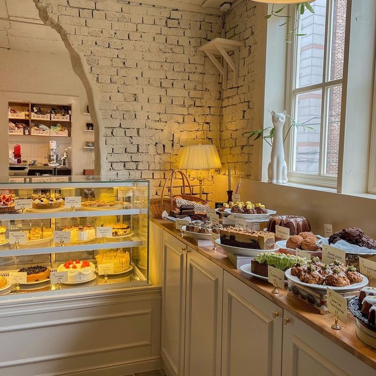 a bakery filled with lots of different types of cakes and pastries on display in front of a brick wall