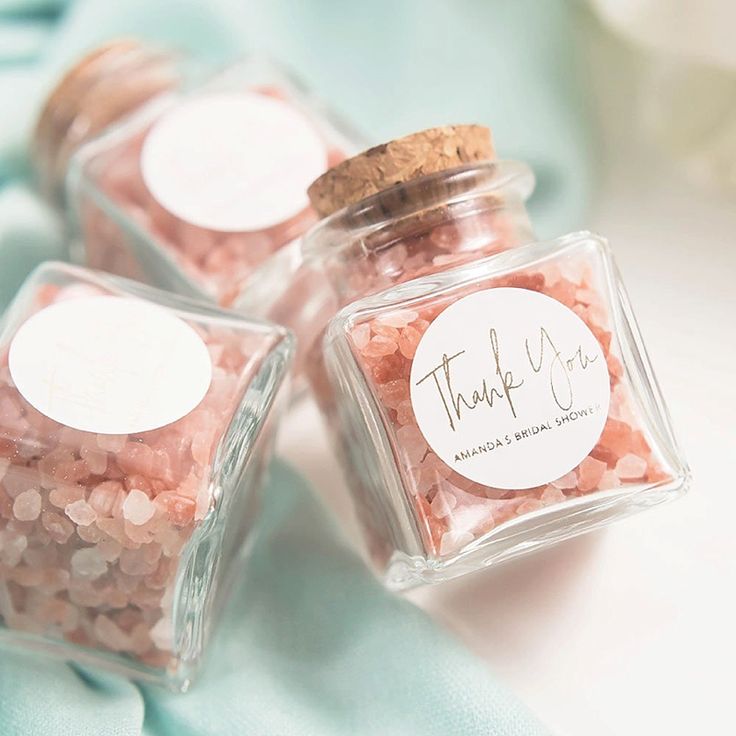 three small jars filled with pink and white confetti on top of a blue cloth