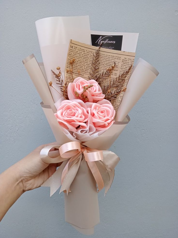 a hand holding a bouquet of pink roses with an old book in the back ground