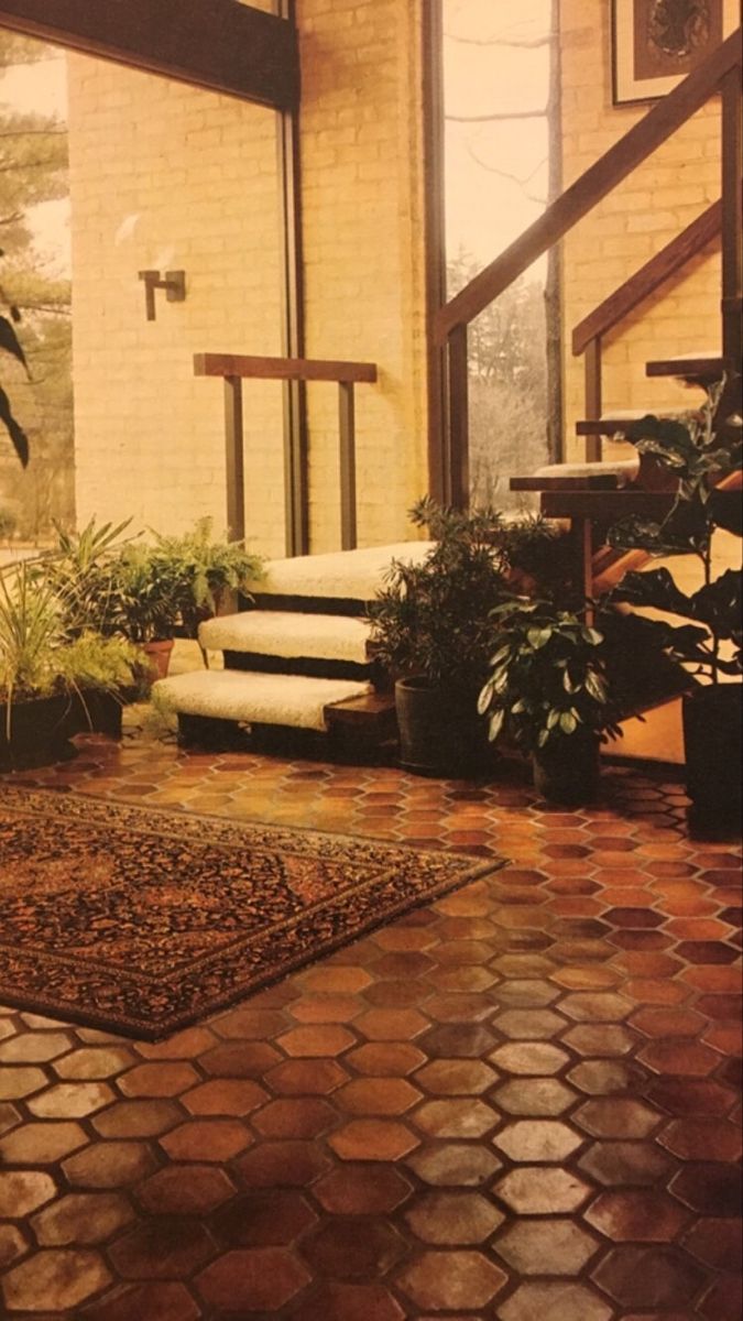 a living room filled with lots of plants next to a stair case in front of a brick wall