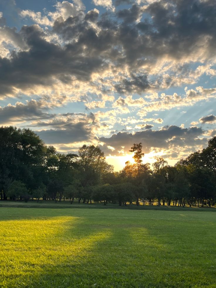 the sun is shining through the clouds in the sky over a field with green grass and trees