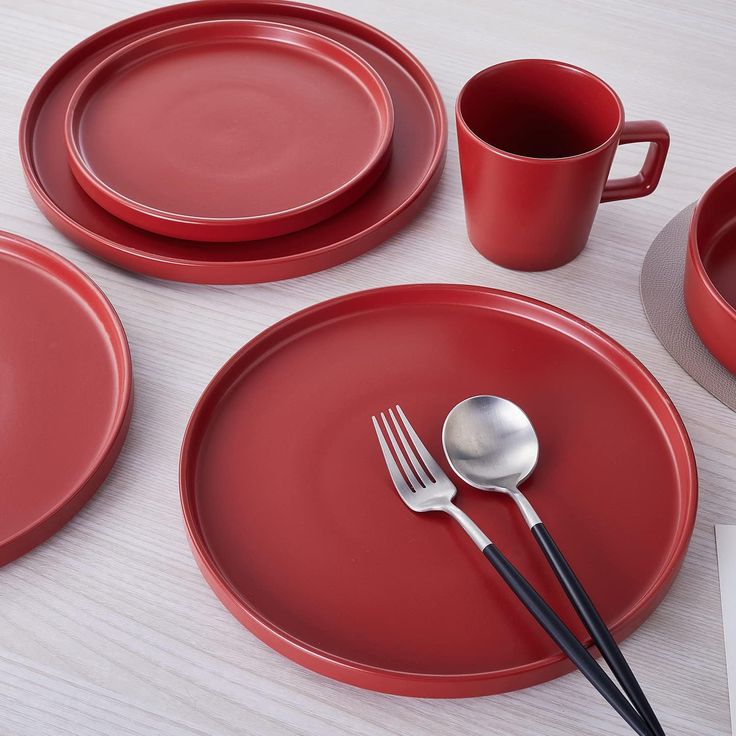 red plates and silverware are arranged on a white table