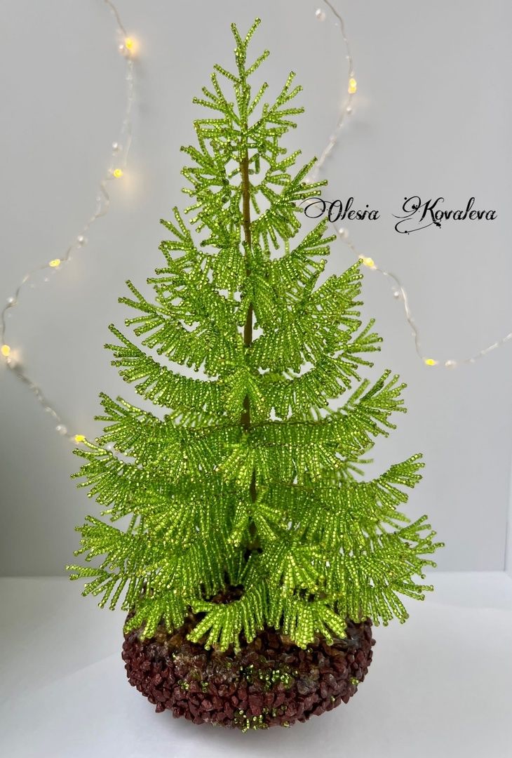 a small green tree sitting in a pot on top of a white table next to a string light