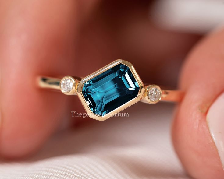 Emerald Cut London Blue Topaz /Topaz Diamond Ring/14k Solid Rose Gold Ring/East West Diamond Ring/November Birthstone/Topaz Engagement Ring  ---------CUSTOM/DUTY-FREE SHIPPING WORLDWIDE, BUYERS DON'T HAVE TO PAY ANY CUSTOM FEES WHILE IMPORTING ------------- Details Made to order Material: 14k/18k gold Color Options: Yellow Gold, White Gold, Rose Gold ★ Center Stone London Blue Topaz, Emerald-cut Size: 5x7mm Approx. Weight (Ct): 0.98 ★ Accent Stones Diamond Round Size: 1.8 mm * 2 Nos. Approx. Weight (Ct): 0.05 ★ 100% Natural Diamond and Gemstones ★ Diamond: Round Brilliant cut, G-H Color, SI Clarity ☂ Shipped with Insured Shipping with 4-7 business days. ➦ 100% Free Returns. ➦ Our Jewelry comes with Lifetime Warranty. (Stone Replacement not included) ✈ We offer free EXPRESS shipping across Luxury Modern Topaz Wedding Ring, Luxury Blue Topaz Emerald Cut Jewelry, Rectangle Topaz Ring, Luxury Modern Topaz Ring With Round Shape, Luxury Emerald Cut Topaz Ring With Diamond Accents, London Blue Topaz Ring Yellow Gold, London Blue Topaz Engagement Rings, Topaz Diamond Ring, Bezel Engagement Ring