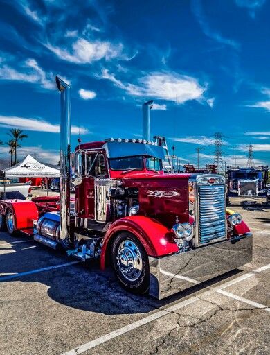 a red semi truck parked in a parking lot next to other trucks and trailers on a sunny day