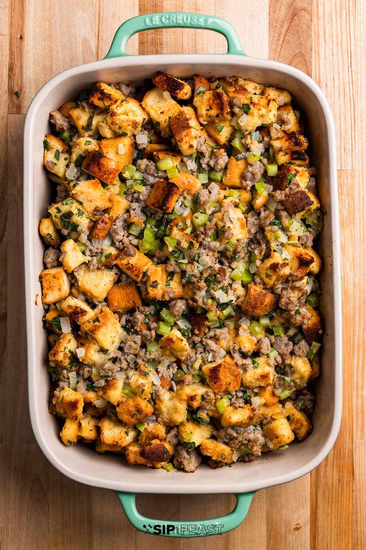 a casserole dish filled with stuffing and vegetables on a wooden counter top, ready to be eaten