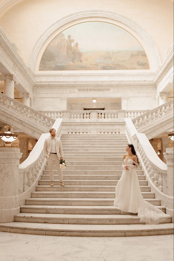 a bride and groom standing on the steps of a grand staircase in an ornate building