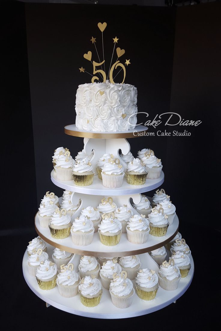 a three tiered cake with white frosting and gold decorations on top is surrounded by cupcakes