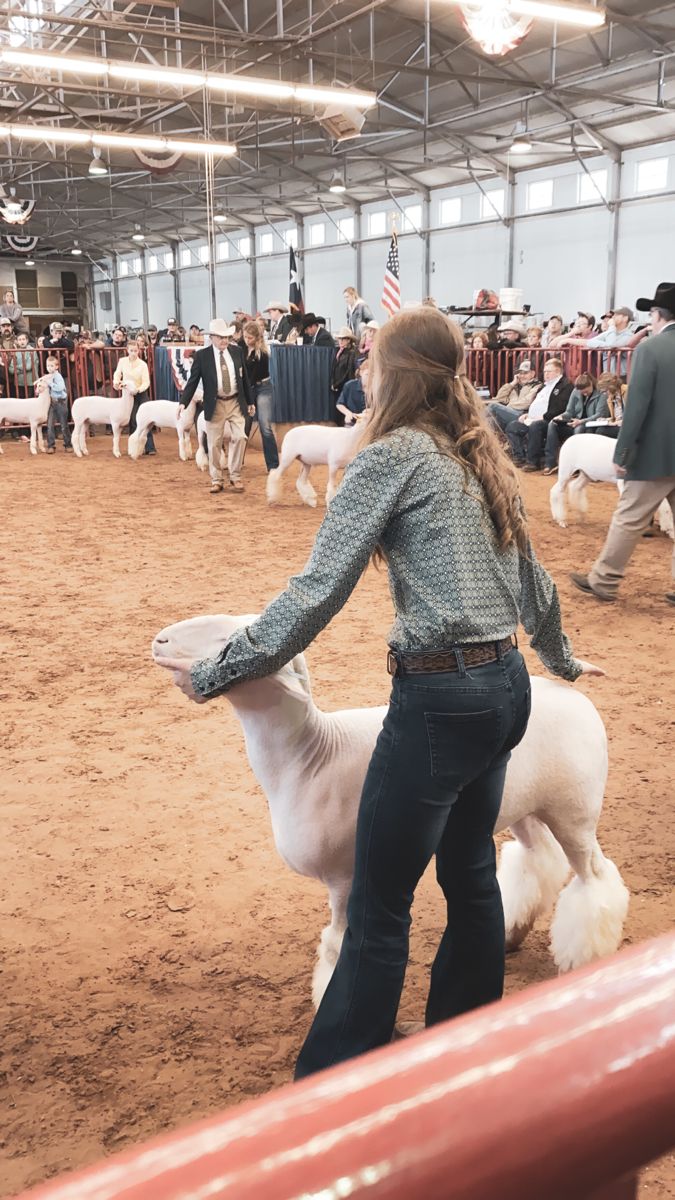 a woman is holding the back of a sheep in an indoor arena with other animals