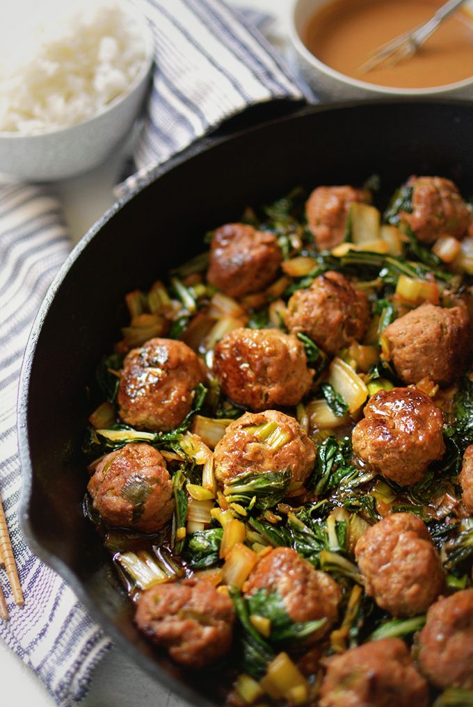 meatballs and vegetables in a skillet next to some rice on a table with chopsticks