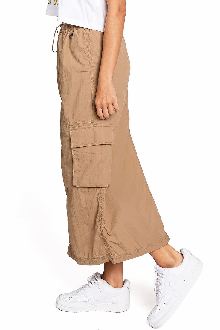 Chic, parachute skirt with an elastic waistband, a drawstring cinch tie and cargo pockets down the sides. Pair it with a graphic tee and sneakers for an effortless streetwear look. CARE | Machine Wash Cold CONTENTS | 100% Nylon MEASUREMENTS | 33"/85 cm Top to Bottom (Size Small) MODEL | 5'8 - wearing a size Small IMPORTED Sporty Spring Cargo Pants With Functional Drawstring, Sporty Spring Cargo Pants With Drawstring, Casual Baggy Cargo Skirt For Spring, Sporty Cargo Pants With Drawstring For Summer, Casual Cotton Cargo Skirt For Summer, Casual Cotton Cargo Skirt For Spring, Sporty Bottoms With Multiple Pockets For Spring, Sporty Spring Bottoms With Multiple Pockets, Casual Relaxed Fit Cargo Pants With Drawstring