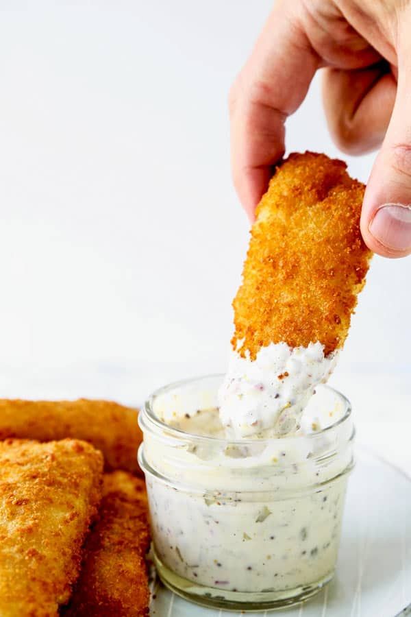 a person dipping something into a small glass jar filled with cream cheese sauce on top of fried fish sticks