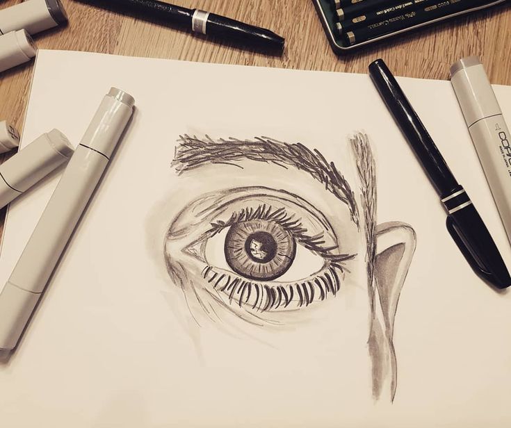 a pencil drawing of an eye and some pens on a piece of paper next to it