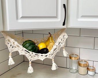 a hammock filled with fruits and vegetables on top of a kitchen counter next to white cabinets