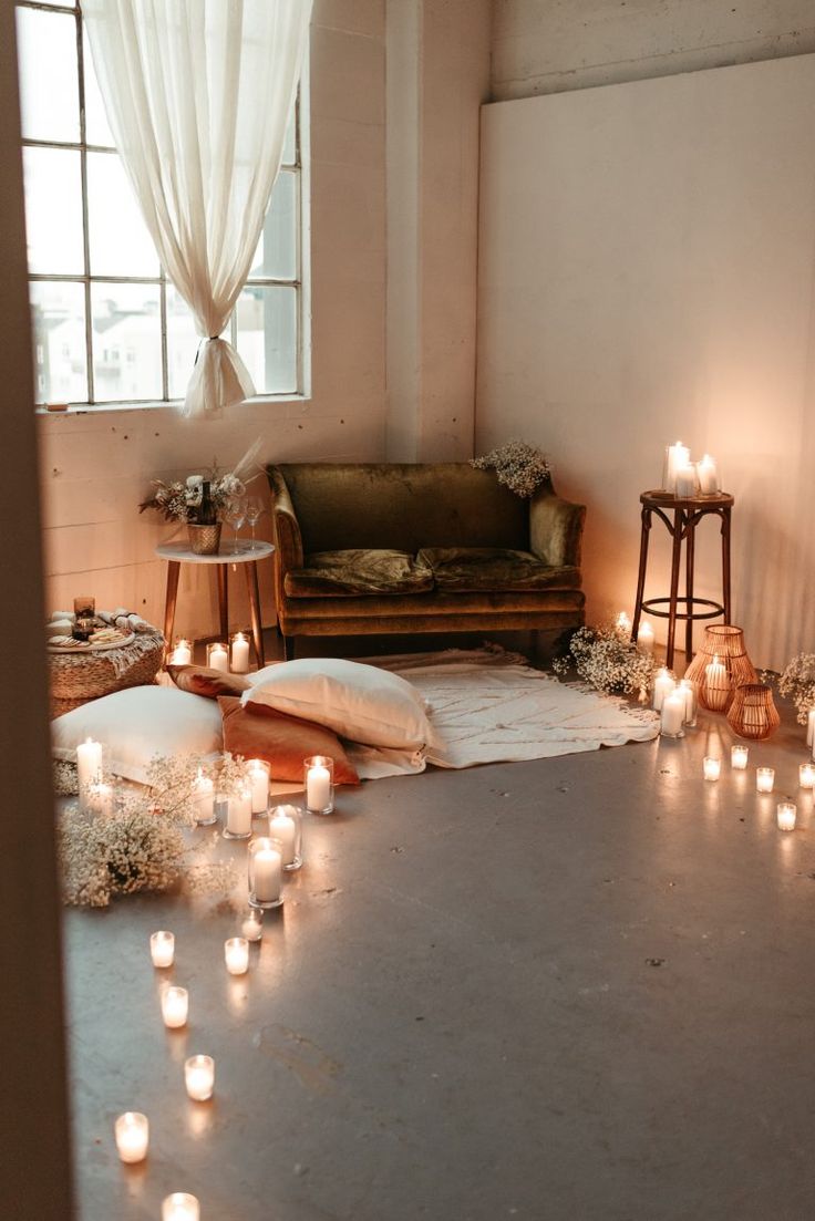 many candles are lit on the floor in front of a couch and window with curtains