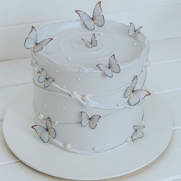 a three layer white cake with butterflies on the icing and frosting, sitting on a plate