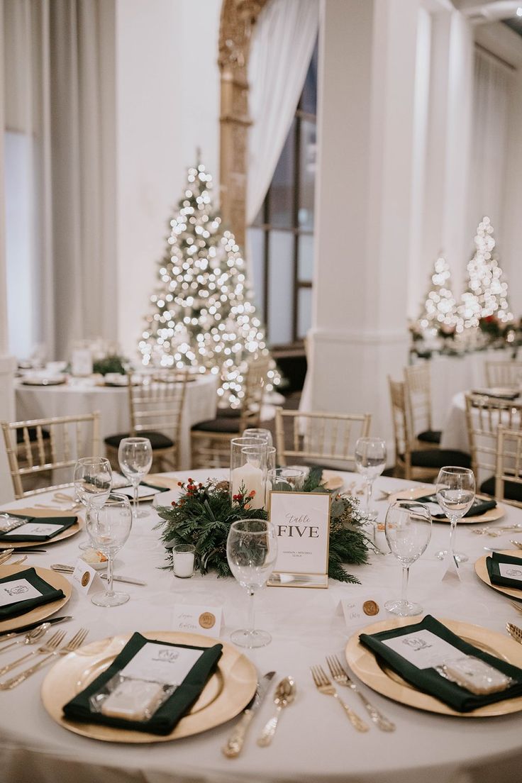 a table set up with place settings and christmas trees in the background at a wedding reception