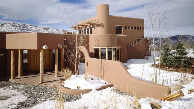 an adobe - style house in the mountains with snow on the ground