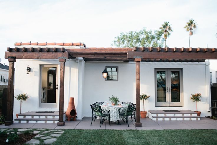 a small white house with an attached patio and table set for two on the front lawn