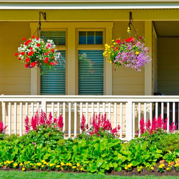 flowers are hanging on the front porch of a house with white railing and flower boxes