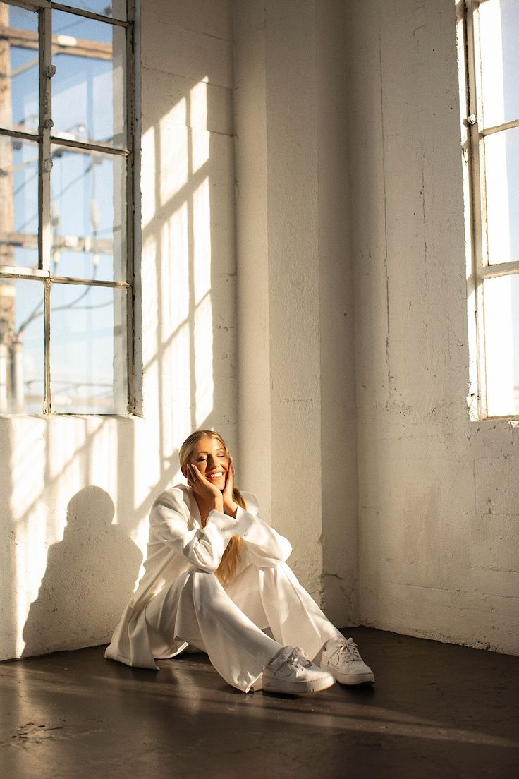 a woman sitting on the floor in front of a window wearing a white suit and sunglasses