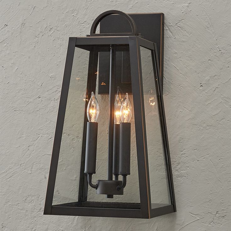 an outdoor wall light with three lights on it's sides and two candles in the middle