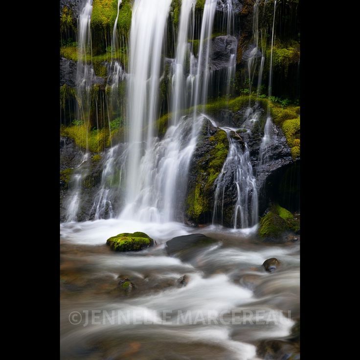 a waterfall with moss growing on the rocks and water running down it's sides