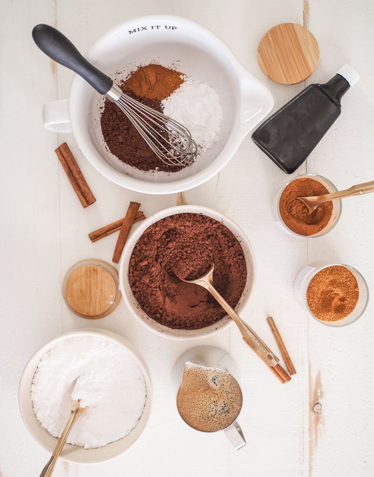 the ingredients for chocolate cake are in bowls and spoons next to each other on a white surface