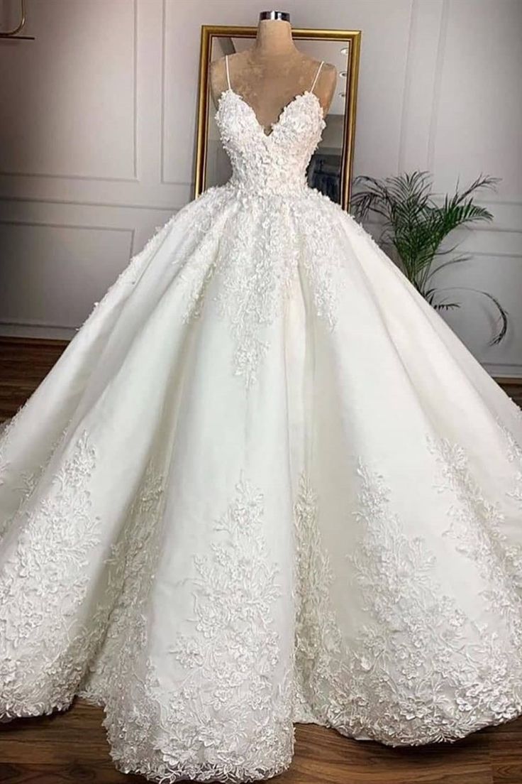 a white ball gown with flowers on the skirt and straps is displayed in front of a mannequin