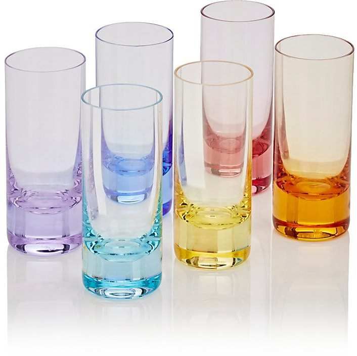 several different colored glasses are lined up on a white surface with one empty glass in the middle