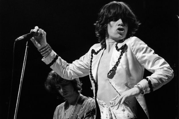 the rolling stones performing on stage with their hands in the air and one person holding a microphone