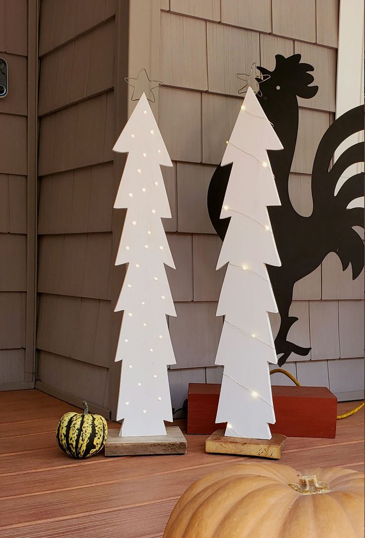 two white christmas trees sitting on top of a wooden table next to a black rooster