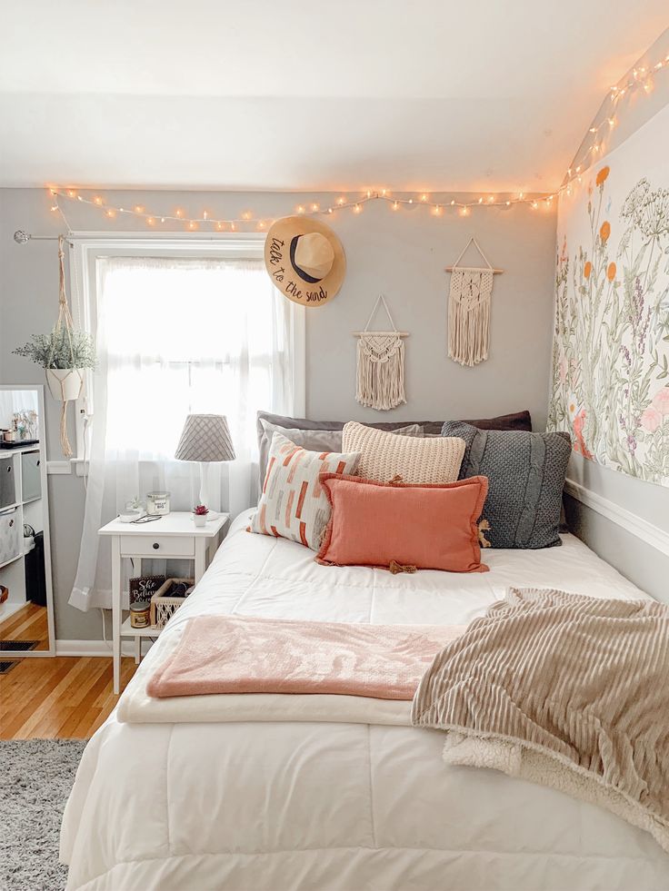 a white bed topped with lots of pillows next to a window covered in string lights